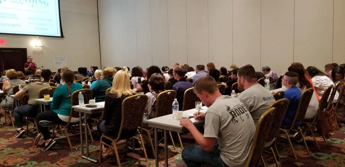 Audience members listening to a presentation in a room with tables